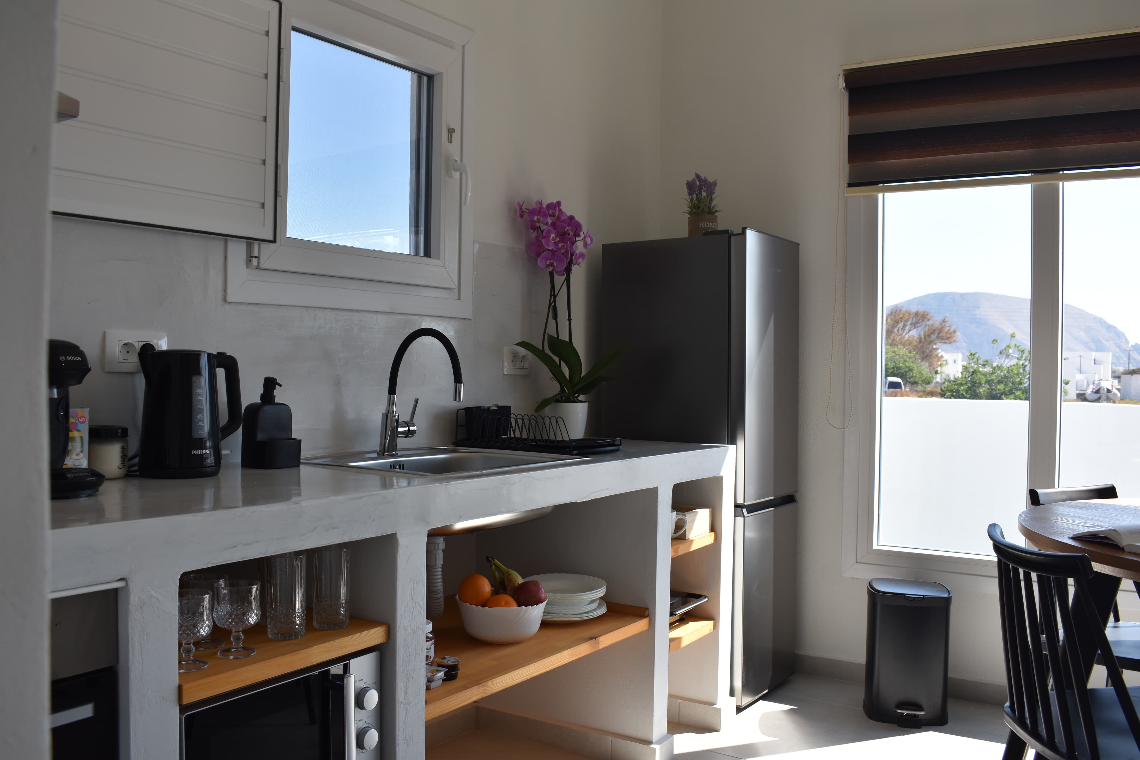 Modern white kitchen with concrete counters, black faucet, stainless steel fridge, and scenic mountain views.