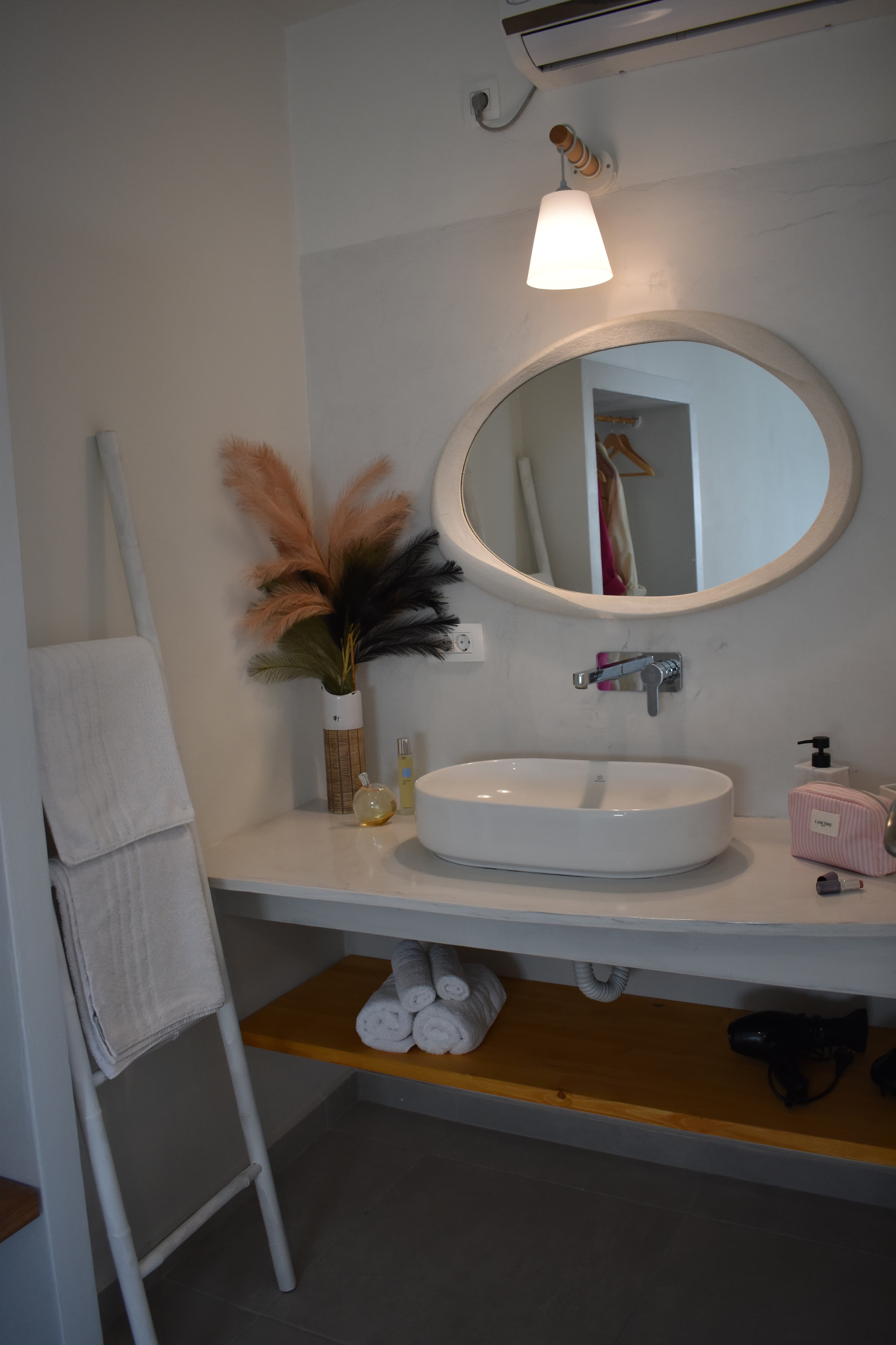 Modern bathroom vanity featuring a white vessel sink, oval mirror, and decorative pampas grass.